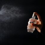 A hand elegantly spritzing perfume from a decorative bottle against a dark background.